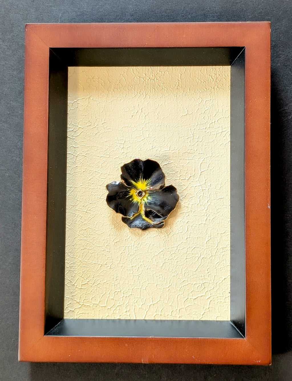 Framed artwork of a black and yellow flower brooch on a textured beige canvas background