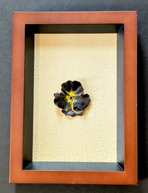 Framed artwork of a black and yellow flower brooch on a textured beige canvas background