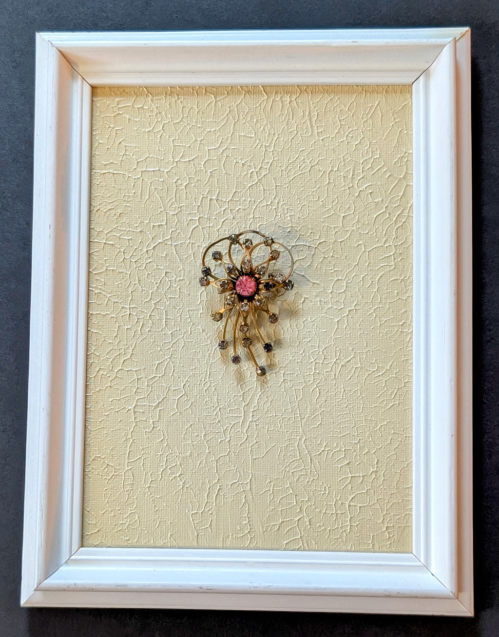 Decorative brooch on textured beige background in a white frame