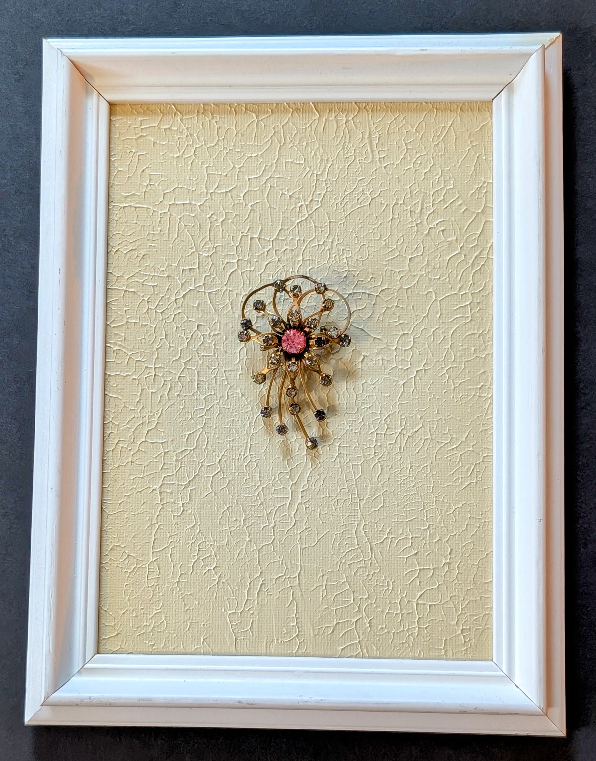 Decorative brooch on textured beige background in a white frame