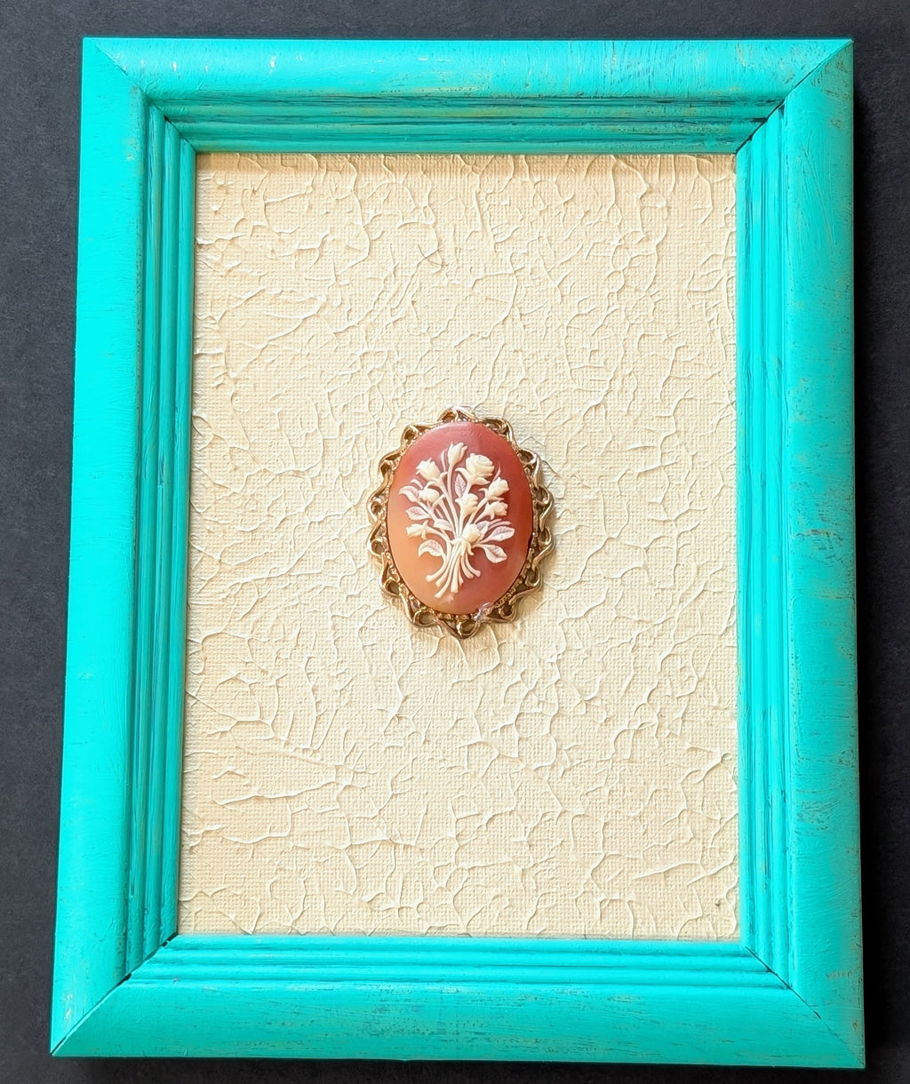 Coral-colored brooch with white design in a turquoise frame on a textured beige background